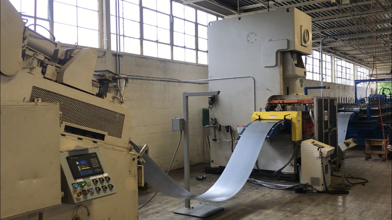 A section of sheet metal is pulled through a roll forming machine on a factory floor